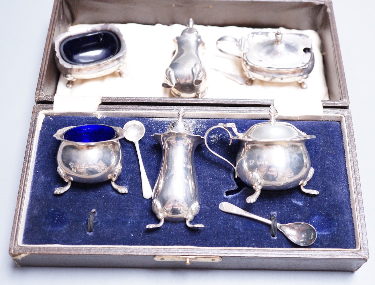 A cased George V silver three piece condiment set, two other silver condiments and a plated condiment.